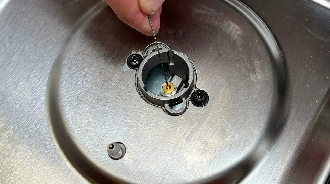 Using a sewing needle to clean clogged gas stove burner port holes